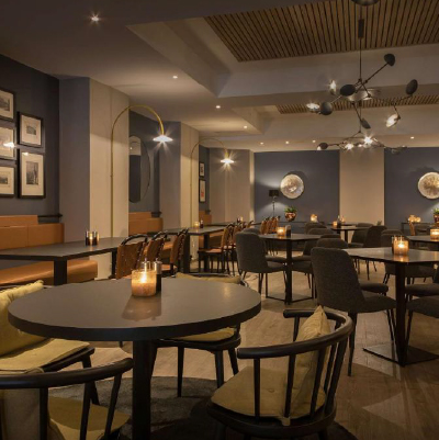 Dining room with round table for four and wooden chairs in front. Candles on the tables.